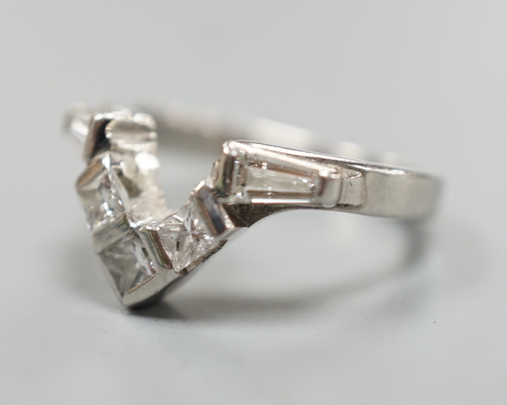 A modern white metal (stamped plat), two stone trapeze cut and three stone princess cut diamond set 'chevron' ring, size I, gross weight 5.3 grams.